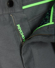 Close-up of the MENS HAYS TWILL PANT by Psycho Bunny, crafted from a gray cotton-blend twill fabric featuring a partially visible zipper. The iconic "PSYCHO" is embroidered in green next to the zipper, with vibrant green accents on the inner fabric flap. The material provides 4-way stretch for enhanced comfort and flexibility.