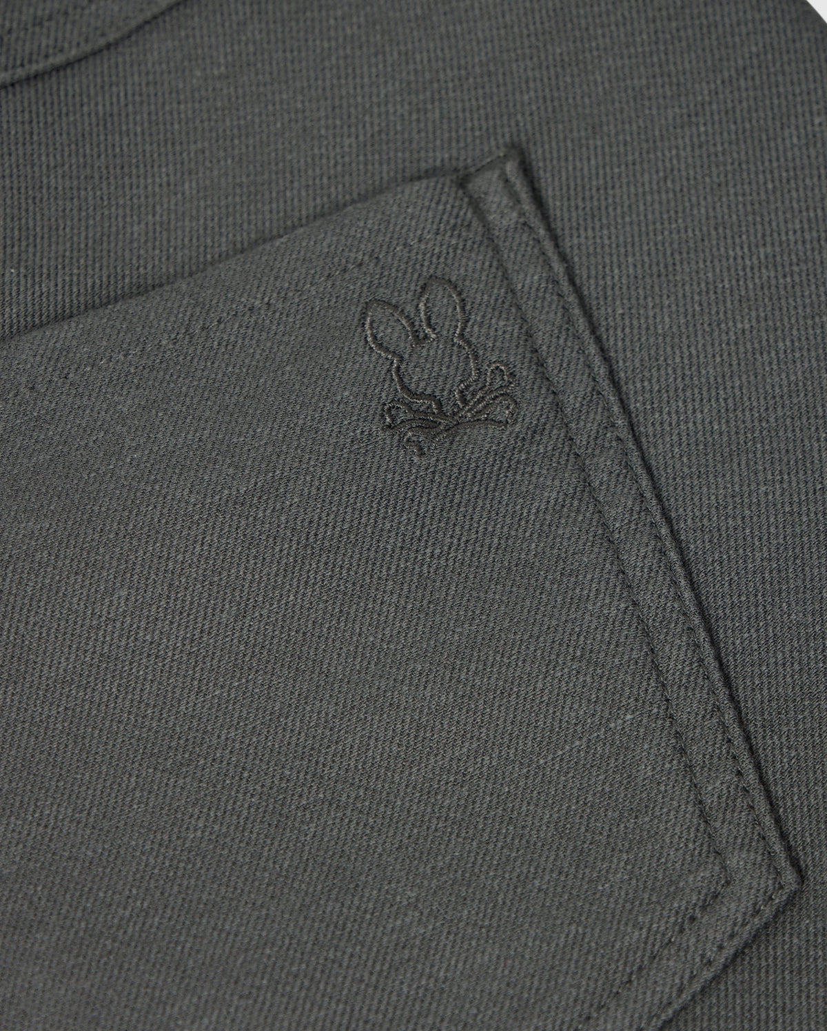 Here's a detailed look at the pocket of the MENS HAYS TWILL PANT - B6P894D200 by Psycho Bunny. The dark grey, regular fit fabric pocket features an embroidered design of a bunny's head and crossed bones. The subtle stitching complements the cotton-blend twill material, which offers 4-way stretch for enhanced comfort and style.