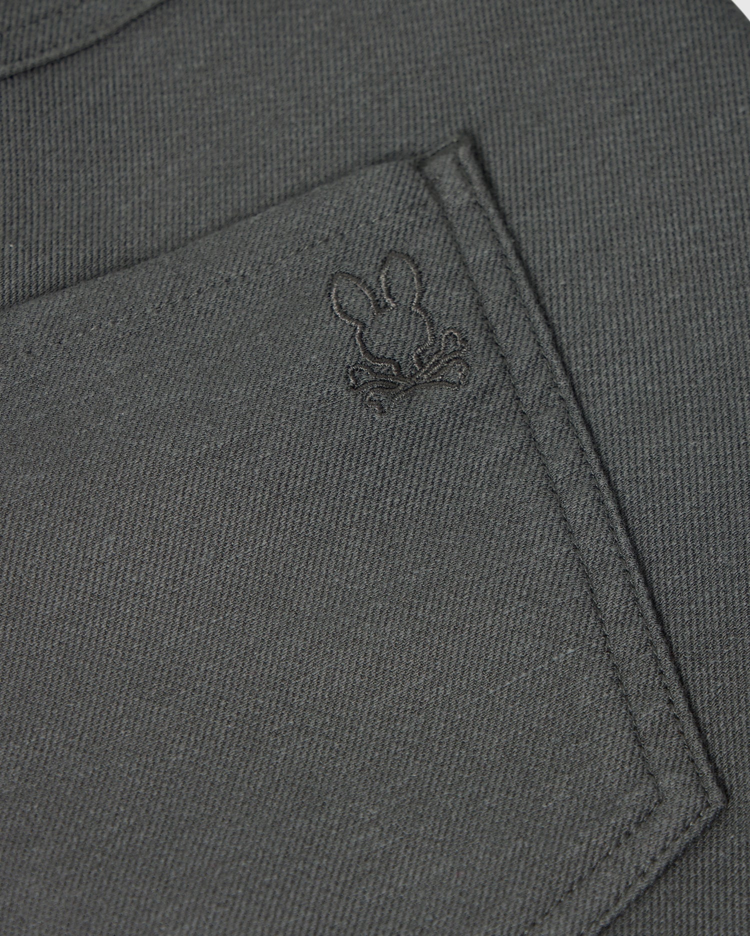 Here's a detailed look at the pocket of the MENS HAYS TWILL PANT - B6P894D200 by Psycho Bunny. The dark grey, regular fit fabric pocket features an embroidered design of a bunny's head and crossed bones. The subtle stitching complements the cotton-blend twill material, which offers 4-way stretch for enhanced comfort and style.