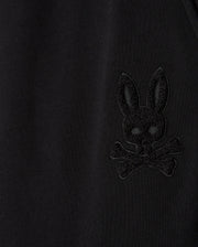 Close-up of the Psycho Bunny MENS PACIFIC CHENILLE JOGGER - B6P972D200 in black, highlighting an embroidered design of a bunny head with crossbones. This casual bottom showcases the stylish high-pile chenille logo patch detail that stands subtly raised from the fabric.