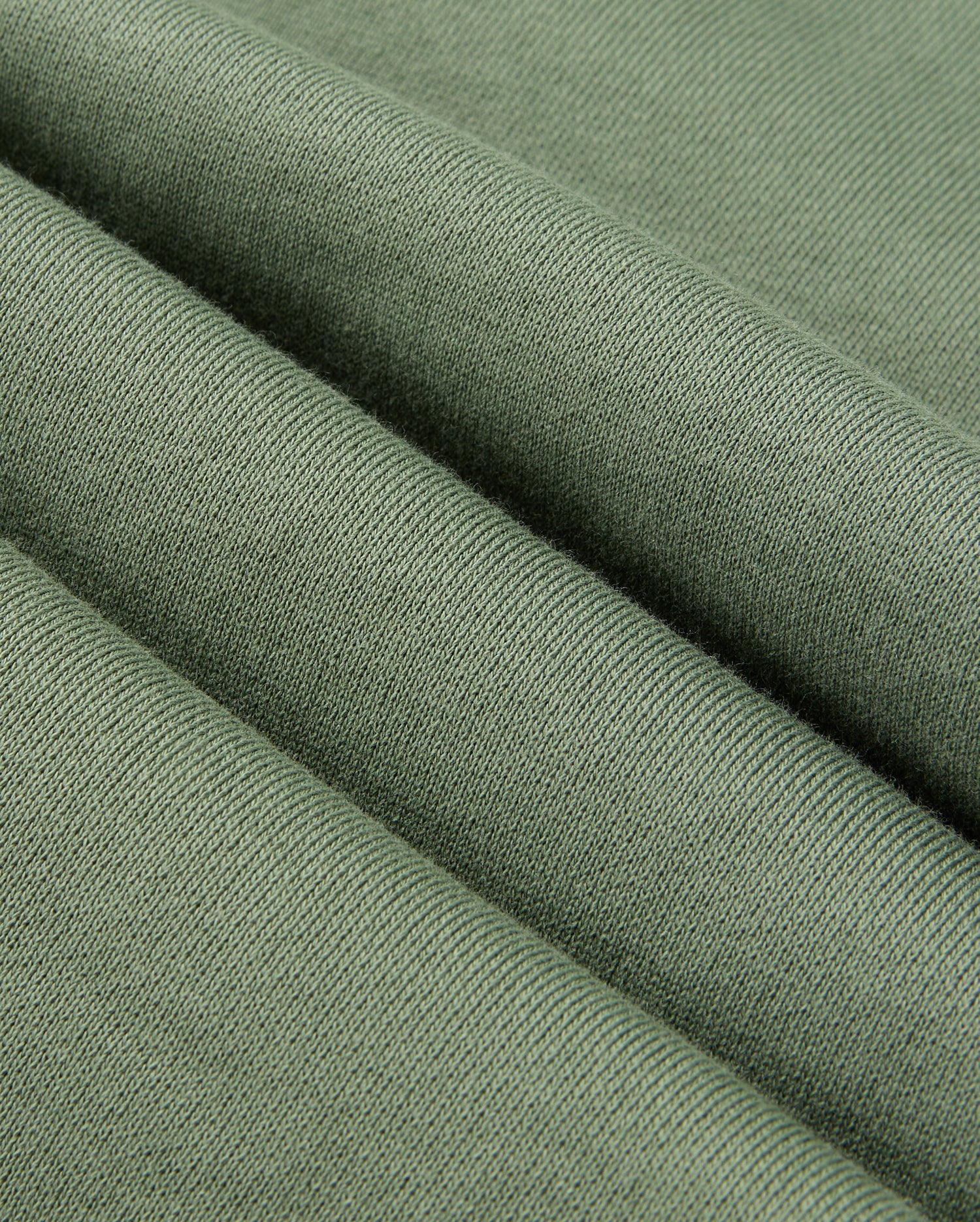 Close-up of green knitted fabric, highlighting its texture and soft appearance with visible weave patterns that evoke the cozy feel of Psycho Bunny's casual bottoms. The fabric is folded into gentle, evenly spaced ridges similar to the smooth drape of the MENS PACIFIC CHENILLE JOGGER - B6P972D200.