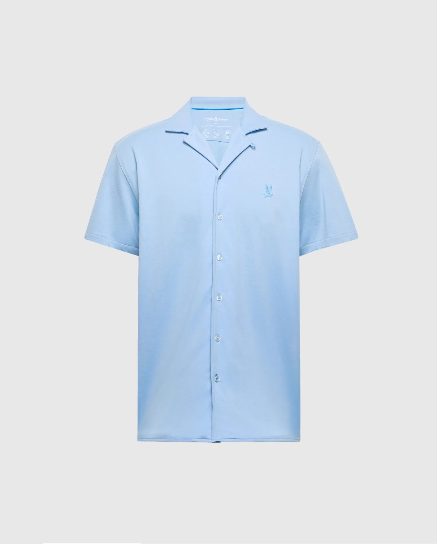 The Psycho Bunny MENS BRYAN CAMP COLLAR SHORT SLEEVE SHIRT in light blue features moisture-wicking performance fabric, a small embroidered chest logo, and a relaxed collar. It is displayed against a plain gray background. Model: B6Q581F200.