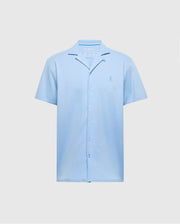 The Psycho Bunny MENS BRYAN CAMP COLLAR SHORT SLEEVE SHIRT in light blue features moisture-wicking performance fabric, a small embroidered chest logo, and a relaxed collar. It is displayed against a plain gray background. Model: B6Q581F200.