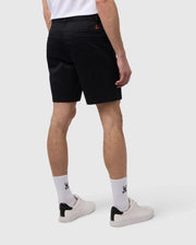 A man wearing black elastic waist shorts (MENS YORK CHINO SHORT - B6R357B200) by Psycho Bunny, white socks with a logo, and white sneakers on a plain background, showing only from the waist down.