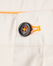 Close-up of a black button on white Psycho Bunny Men's York Chino Shorts with distinctive orange stitching detail and embossed text. The button is securely sewn to the garment.