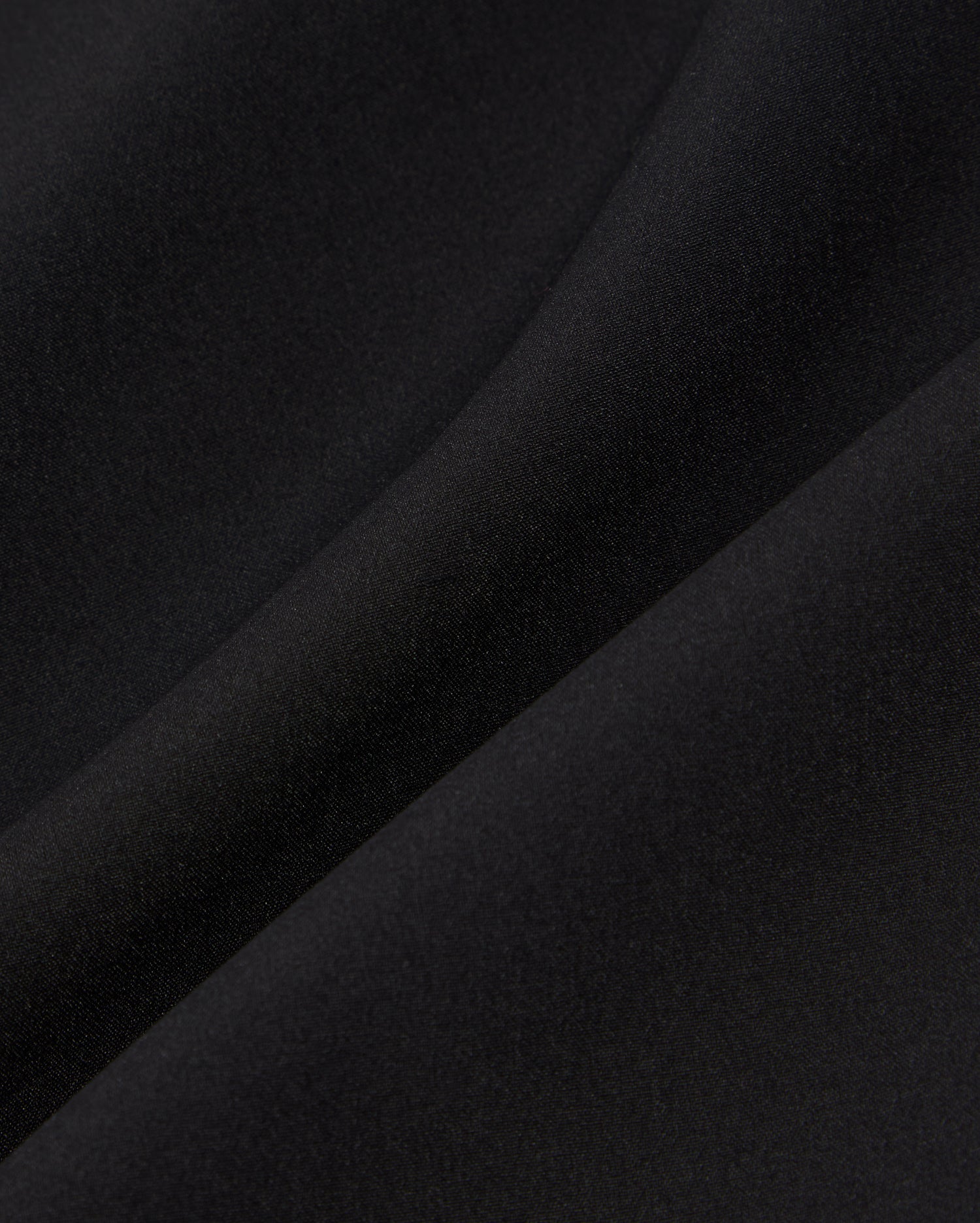 Close-up of a smooth, black fabric showing subtle light reflections and a gentle fold. The texture appears soft and even, indicating a fine, high-quality material often used in the Psycho Bunny MENS SONTERRA STRIPE SPORT SHORT - B6R464C200 for its quick-drying and breathable properties.