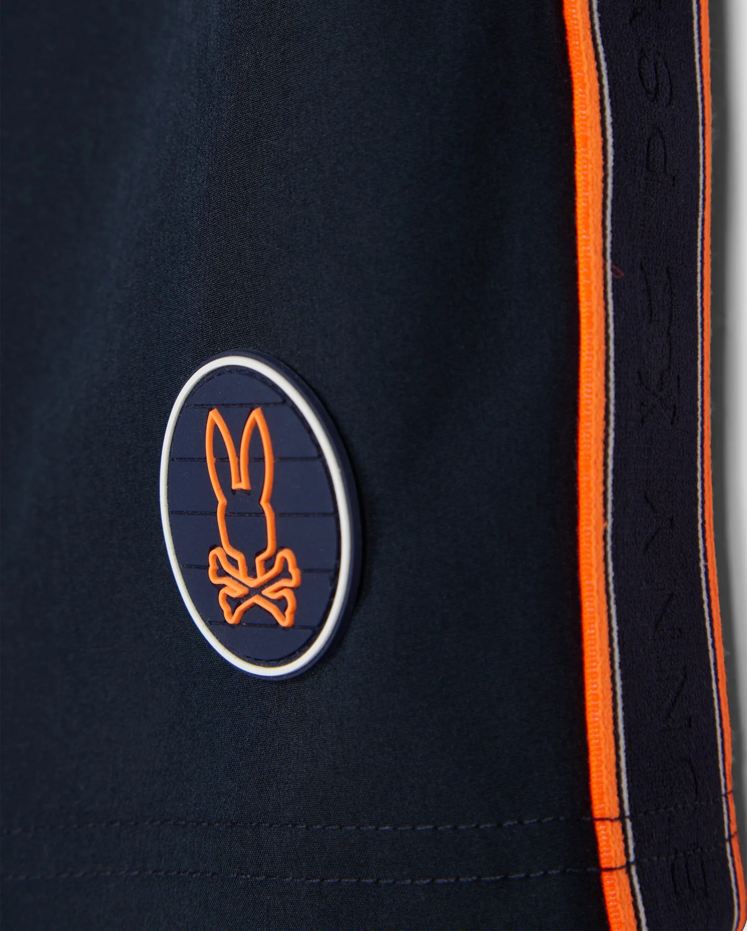 A logo on a pair of Psycho Bunny MENS SONTERRA STRIPE SPORT SHORT - B6R464C200 made from quick-drying, stretch fabric in blue and orange.