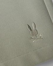 Close-up of a Psycho Bunny honeycomb fabric with a small, intricately embroidered silver rabbit holding a branch, stitched near the edge of the material.