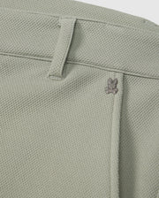 Close-up of a light green Psycho Bunny honeycomb fabric with a subtle texture, featuring a small metal bunny logo near the seam of a pocket.