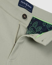 Close-up of a beige Psycho Bunny MENS SHIRO KNIT HONEYCOMB SHORT - B6R567C200 jacket with a partially unzipped front, revealing a vibrant honeycomb fabric lining patterned with green and navy blue bunnies. The collar tag and front button are also visible.
