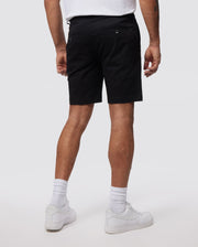 A person is standing facing away from the camera, wearing a white t-shirt, Psycho Bunny MENS HAYDEN SHORT - B6R757ARCE in black, white socks, and white sneakers. The slim fit ensemble is crafted from breathable cotton. The background is plain and neutral.