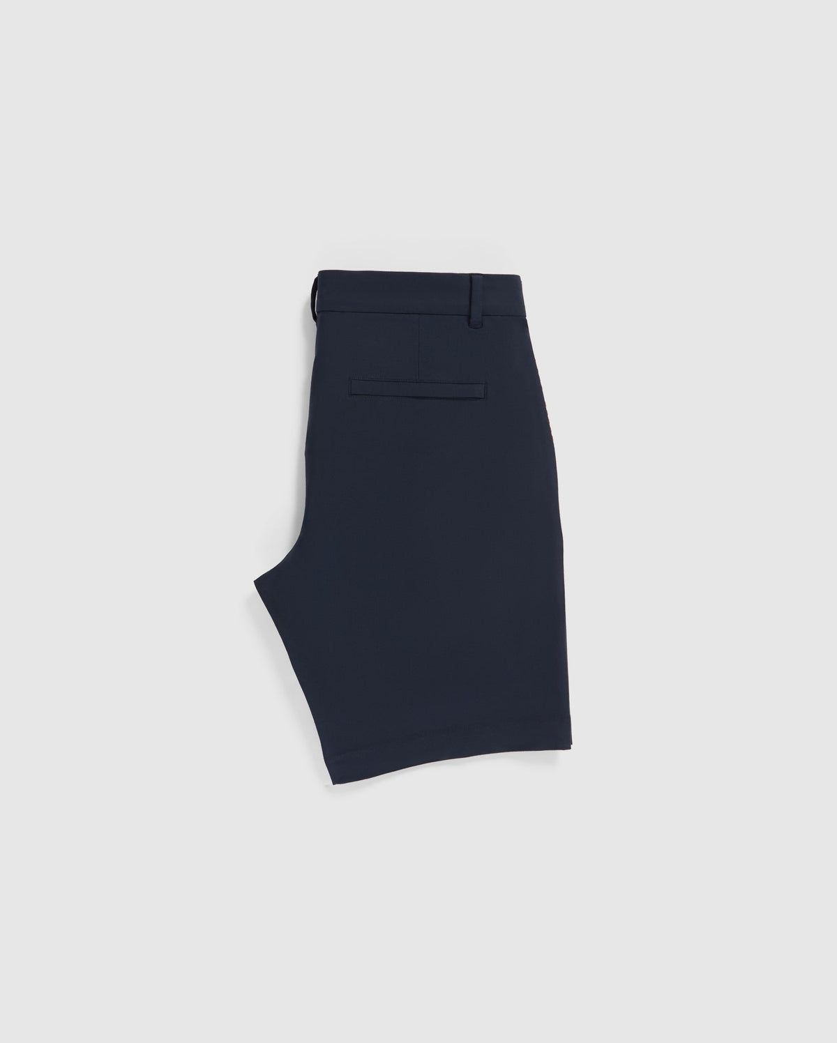 A pair of Psycho Bunny MENS GABLE REGULAR FIT SPORT SHORT - B6R761ARCN is folded flat and viewed from the side, showcasing the waistband, a belt loop, and a single back pocket with a horizontal slit design. Made from durable stretch cotton-nylon, these shorts also feature a hidden zip pocket for added functionality. The shorts have a clean, minimalist appearance.