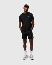 A person wearing a black T-shirt, polyester sport shorts from Psycho Bunny (MENS MANSFIELD SPORT SHORT - B6R807D200), and a black cap stands against a plain background. They are also wearing white sneakers and white socks, with their hands in their pockets.
