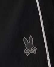 Close-up of the MENS MANSFIELD SPORT SHORT - B6R807D200 by Psycho Bunny in black polyester fabric, showcasing a small logo of a rabbit head above crossed bones. This whimsical take on the traditional skull and crossbones design is accentuated by its perforated texture and white accents on the side, providing a regular fit.
