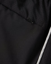 Close-up of a black polyester garment designed by Psycho Bunny, showcasing a subtle, perforated pattern and a partially visible zipper. The fabric exhibits a smooth texture with a hint of shine, highlighted by the MENS MANSFIELD SPORT SHORT style - B6R807D200. It features Psycho Bunny's signature regular fit adorned with a white stripe along the lower edge.