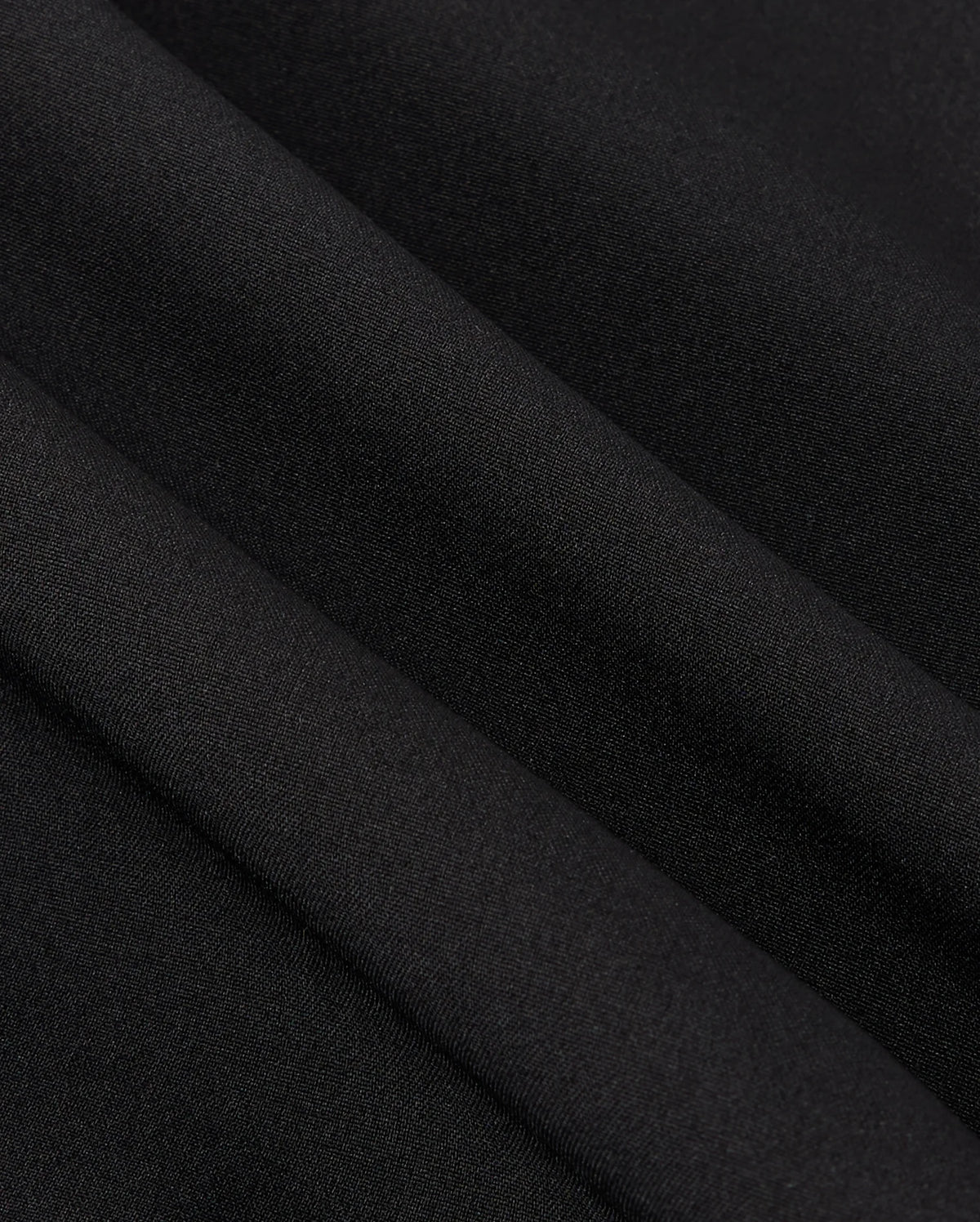 Close-up of smooth, black polyester fabric with visible folds, creating soft shadows and a subtle texture reminiscent of the MENS MANSFIELD SPORT SHORT - B6R807D200 by Psycho Bunny.