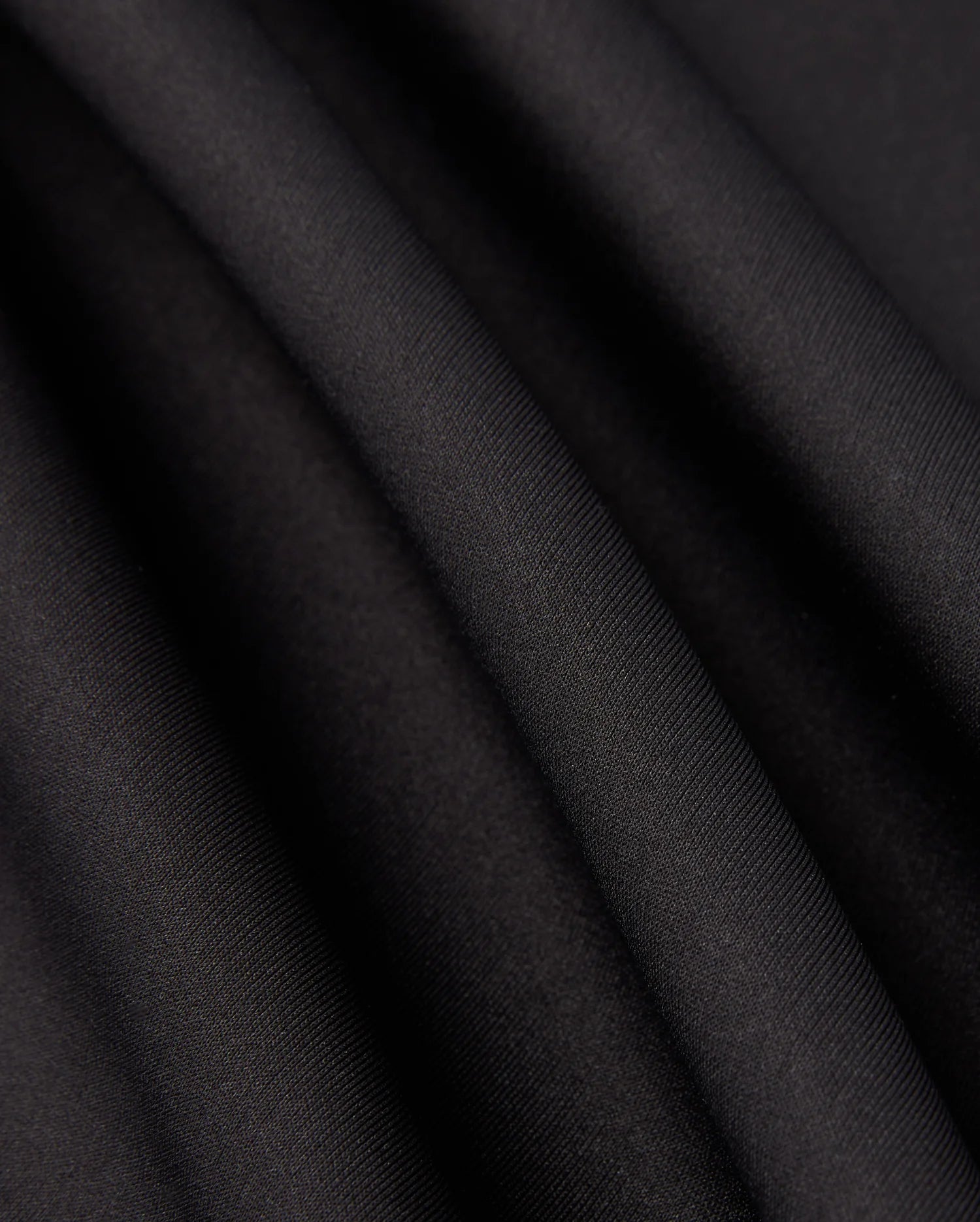 Close-up of the Psycho Bunny MENS LAURIER 1/4 ZIP HOODIE - B6S149D200 in black, crafted from cotton jersey fabric with soft, flowing folds and a smooth texture. The hoodie exudes an elegant, slightly reflective quality, embodying an athleisure aesthetic as it captures light along its gentle curves.