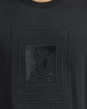 Close-up of the Psycho Bunny black shirt, MENS OAK CITY CREW NECK - B6S274E200, crafted from premium quality fabric and featuring a distinctive embossed design: a silhouette of a rabbit head above crossed bones, framed within geometric borders. This lightweight crew neck shirt is enhanced with raised embroidery for added texture and style.