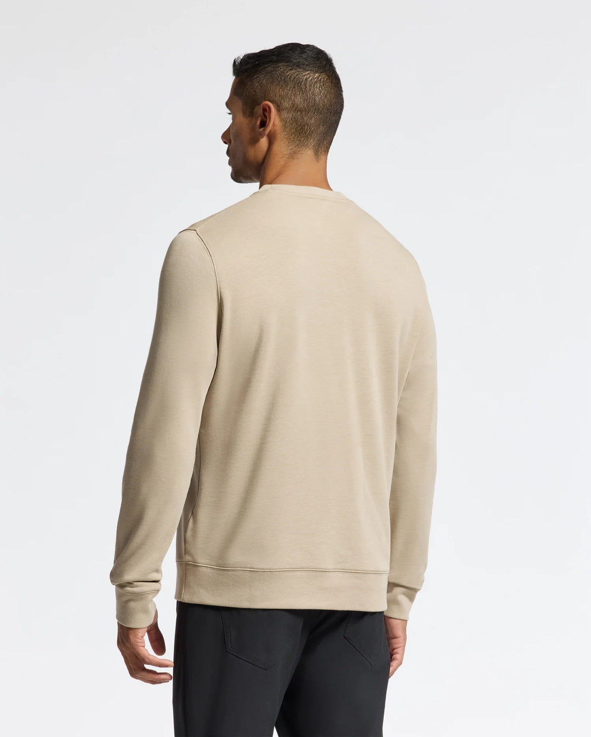 A person wearing a Psycho Bunny Men's Oak City Crew Neck - B6S274E200 sweater and black pants is standing with their back to the camera. The background is a plain white wall, accentuating the elegance of their outfit.