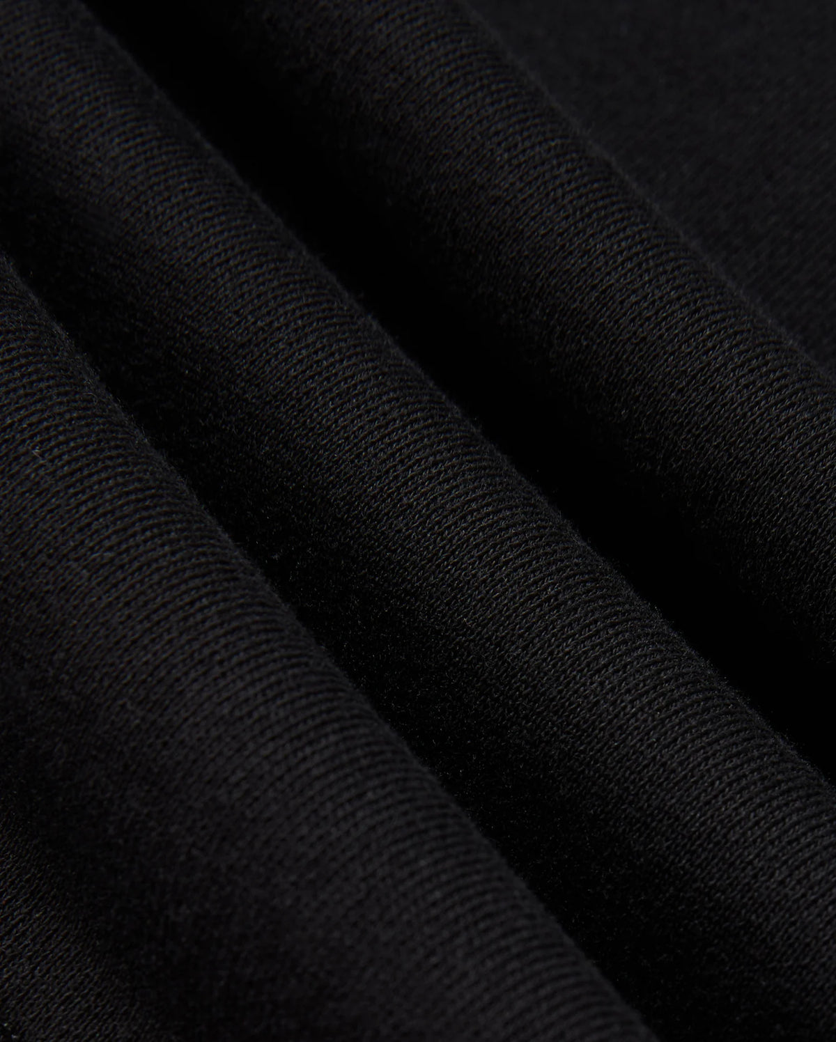 A close-up of the folded fabric reveals its textured and soft surface, evoking the feel of a premium cotton jersey. The black material appears smooth with a slight ribbed effect, and the gentle folds create subtle shadows and depth. This expertly crafted fabric is part of the Psycho Bunny MENS KINGSTON SWEATSHIRT (B6S480D200), showcasing intricate 3D embroidery details.