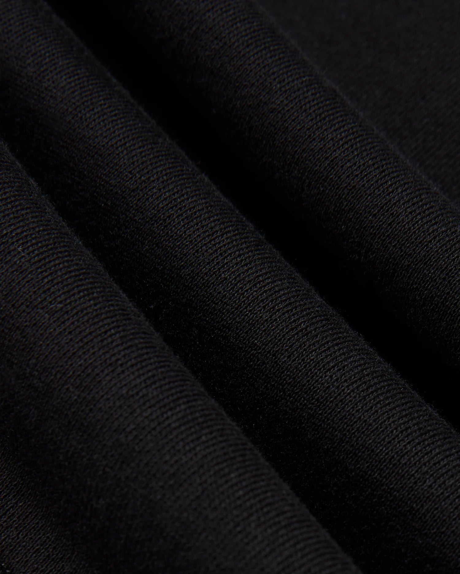 A close-up of the folded fabric reveals its textured and soft surface, evoking the feel of a premium cotton jersey. The black material appears smooth with a slight ribbed effect, and the gentle folds create subtle shadows and depth. This expertly crafted fabric is part of the Psycho Bunny MENS KINGSTON SWEATSHIRT (B6S480D200), showcasing intricate 3D embroidery details.