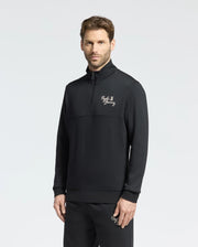 A man with short hair and a beard wears Psycho Bunny's black MENS DESERT 1/4 MOCK ZIP - B6S488F200 pullover, featuring an embroidered wordmark logo, and matching 100% cotton pants against a plain white background.