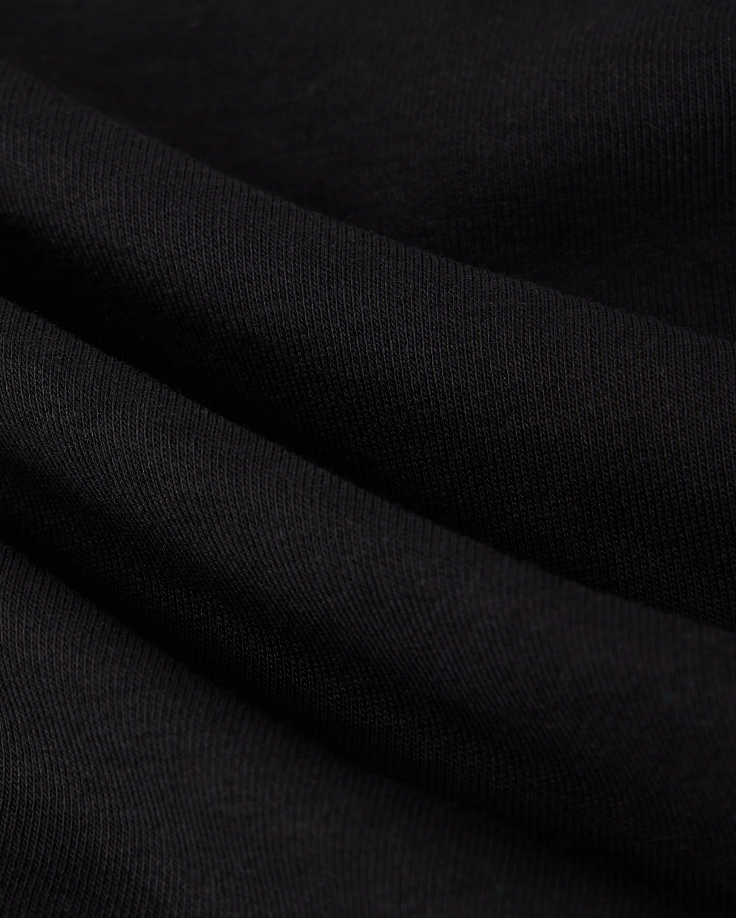A close-up image reveals the black fabric of the MENS COURTSIDE SWEATSHIRT - B6S688C200 by Psycho Bunny, showcasing a soft, slightly wavy texture with a visible weave pattern. The smooth and stretchy material features subtle shadows that enhance its folds, offering a tennis-inspired elegance reminiscent of its design.