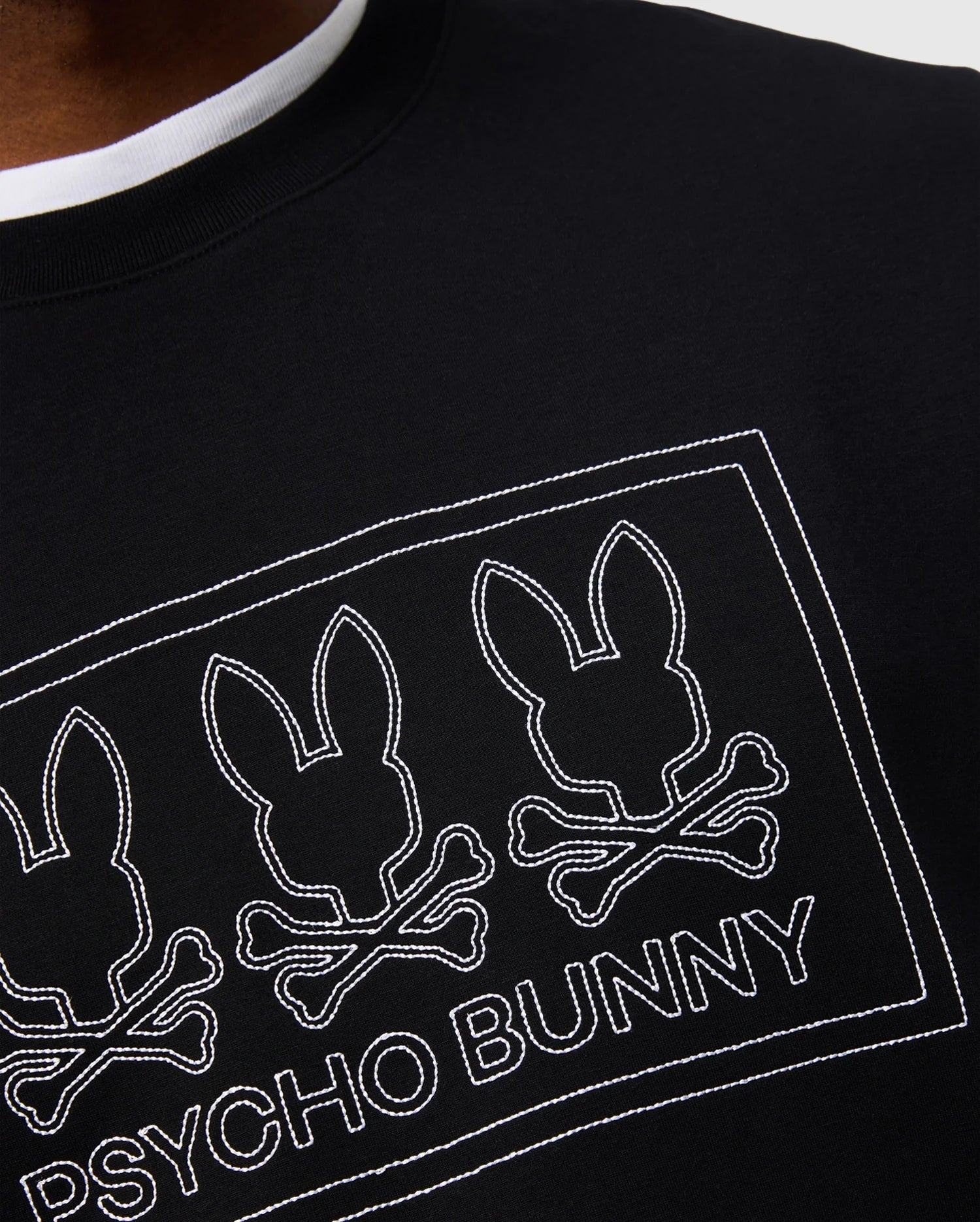 Close-up of the MENS TACOMA MODAL SWEATSHIRT from Psycho Bunny, showcasing a black garment adorned with a design of three stylized bunny heads and crossbones, outlined in white. Made from premium modal fabric, the words "Psycho Bunny" are featured below the design for a touch of luxurious comfort and style.