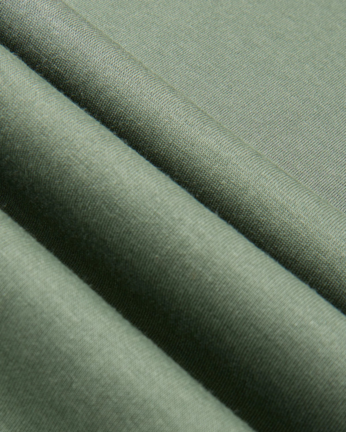 Close-up of the Psycho Bunny MENS TACOMA SWEATSHIRT - B6S927D200 in green fabric, showcasing its soft texture and gentle folds. The lightweight material appears smooth and has a subtle sheen, indicating a fine weave.