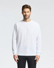 A man with short hair and a beard stands against a plain background, wearing the Psycho Bunny MENS TAYLOR PIQUE LONG SLEEVE TEE in white and black pants. He has a neutral expression, his arms relaxed at his sides, while subtle embroidered bunnies enhance his look.