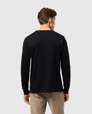 A person with brown hair, wearing a black Psycho Bunny MENS ALBERTON LONG SLEEVE TEE - B6T867D200 and khaki pants, stands facing away against a light gray background.