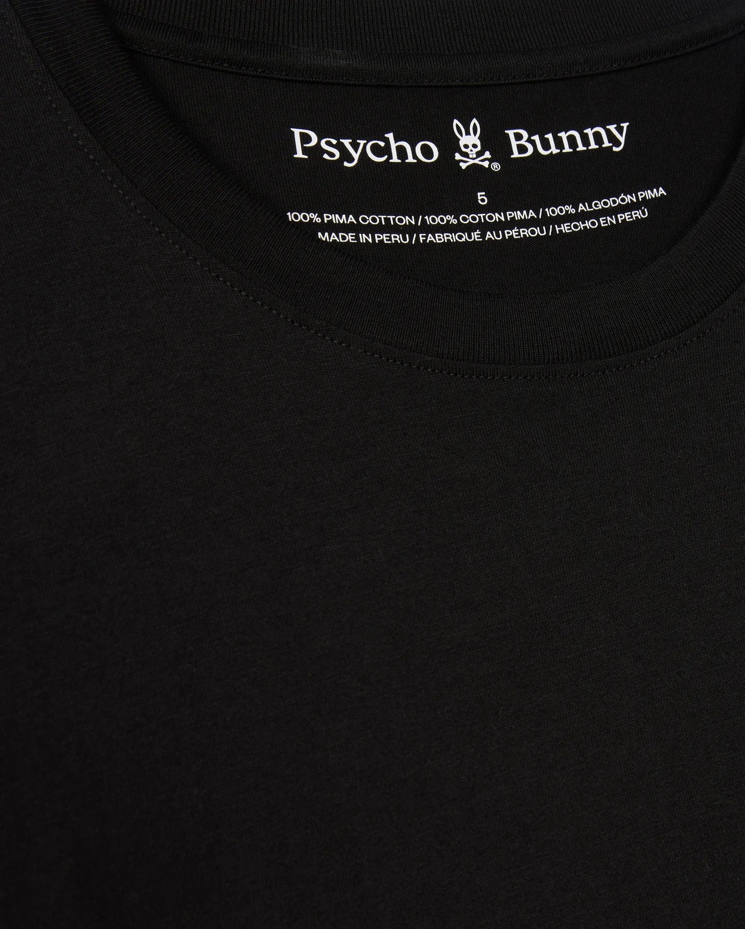 A close-up of the black Psycho Bunny Men's Alberton Long Sleeve Tee – B6T867D200 highlights its label. This fashion masterpiece features the "Psycho Bunny" name alongside a bunny logo and is detailed in white text: "100% Pima Cotton," "Made in Peru," and size "5".