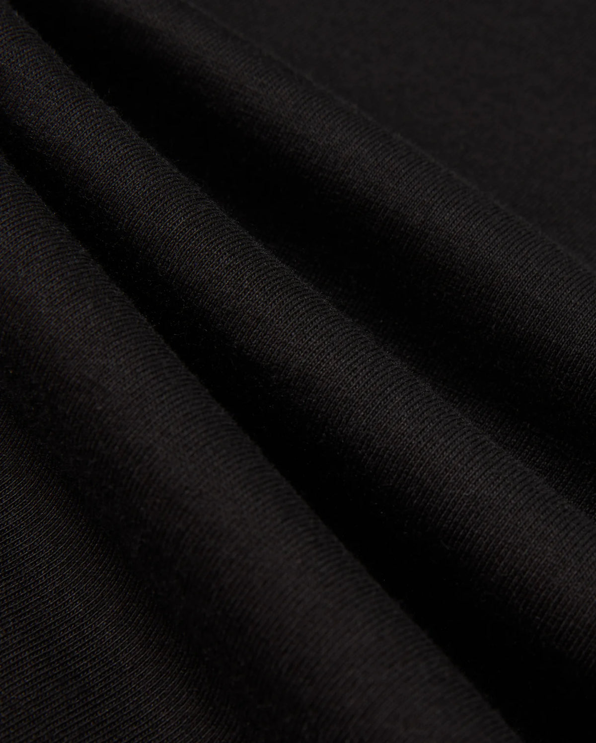 Close-up of the black Pima cotton fabric folds from the Psycho Bunny MENS ALBERTON LONG SLEEVE TEE - B6T867D200, showcasing a smooth, soft texture and fine weave. The wrinkles create subtle shadows, highlighting the material's flexibility and quality—truly a fashion masterpiece.