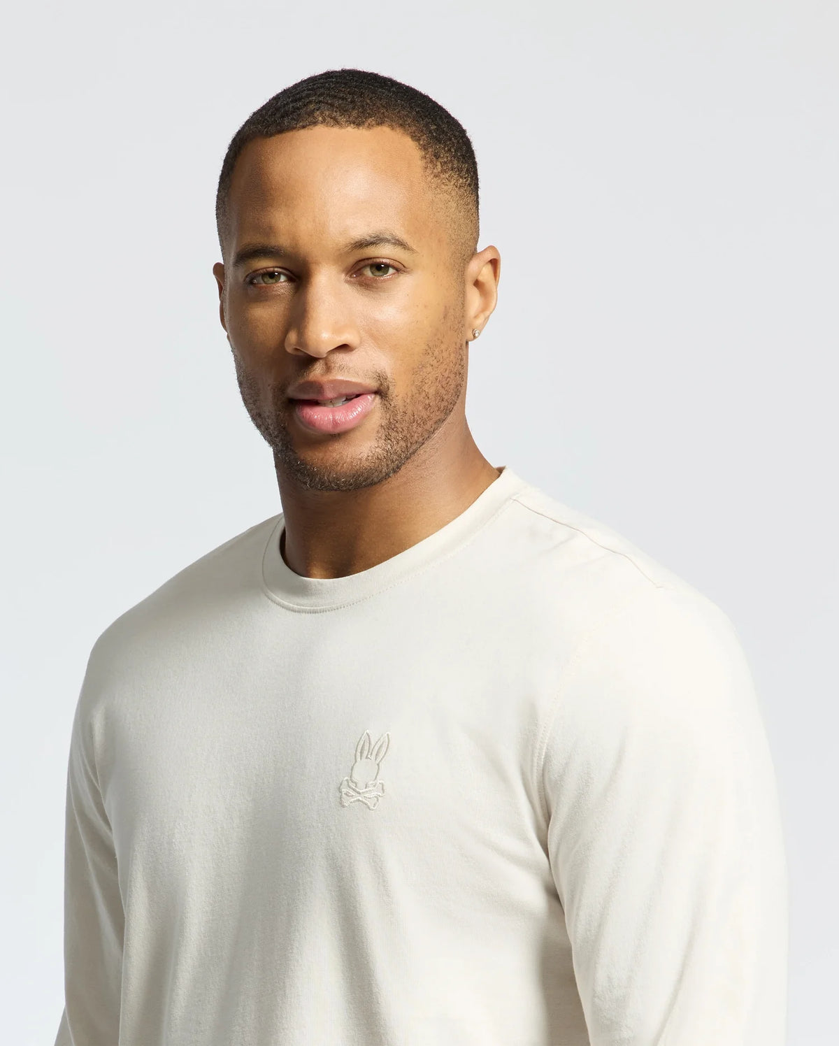 Man wearing a light-colored Psycho Bunny MENS ALBERTON LONG SLEEVE TEE - B6T867D200 with a small embroidered logo against a neutral background.