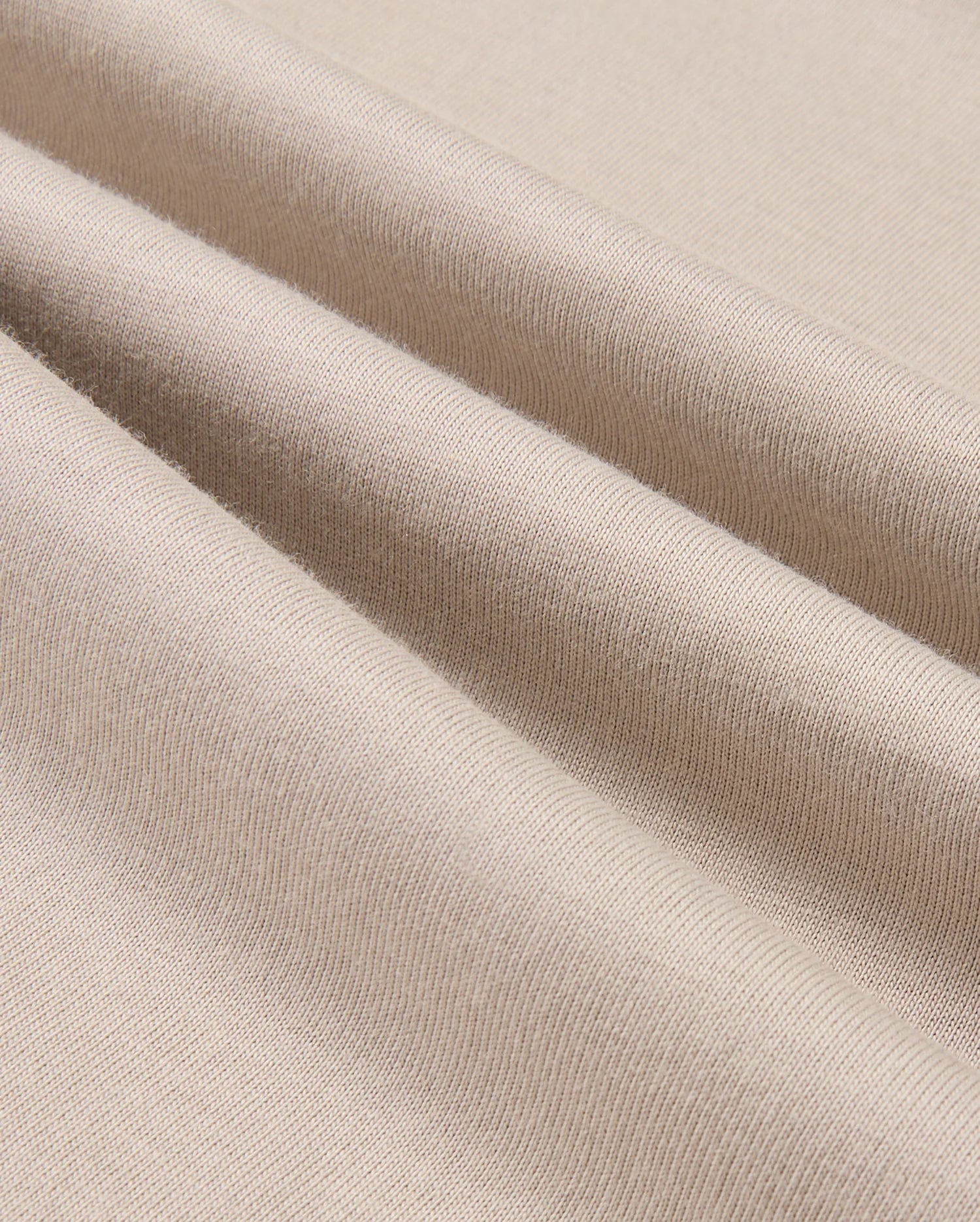 A close-up of the MENS ALBERTON LONG SLEEVE TEE - B6T867D200 by Psycho Bunny highlights the beige fabric elegantly folded to showcase its smooth texture and fine weave. This Pima cotton tee exemplifies flexibility and softness, making it the perfect choice for a luxurious layering piece.