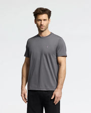 A man with short brown hair and facial hair is wearing a versatile Psycho Bunny MENS CLASSIC CREW NECK TEE (B6U014F200) in gray, crafted from soft pima cotton with a small logo on the chest. He pairs it with black pants and stands against a plain white background, gazing neutrally at the camera.