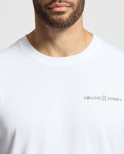 A person wearing the MENS LONGMONT GRAPHIC TEE - B6U194E200 by Psycho Bunny, featuring a plain white Pima cotton design with the signature logo on the chest. The neutral background perfectly complements this casual men's graphic tee.