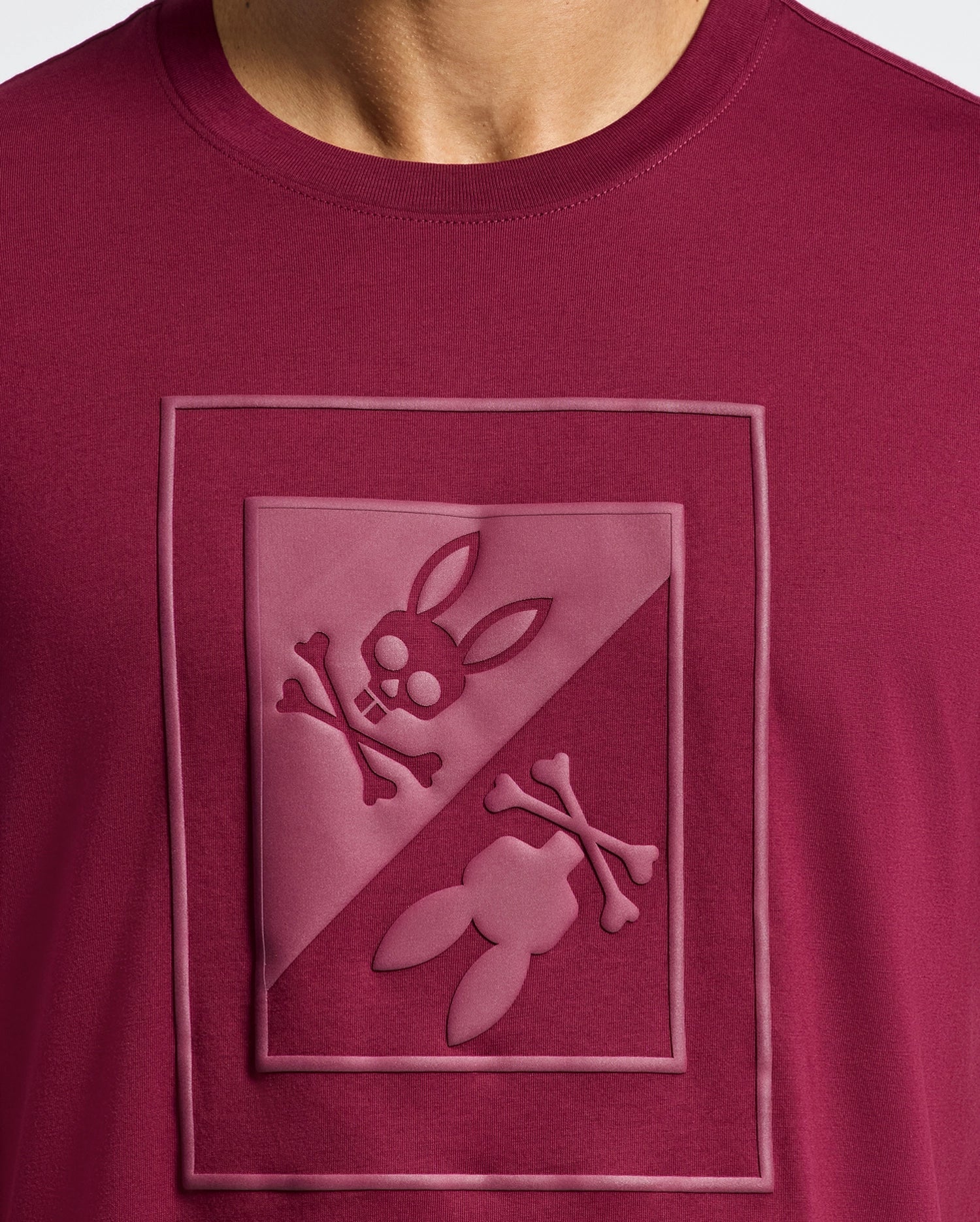 Close-up of the Psycho Bunny Men's Dotsero Graphic Tee - B6U197E200 in maroon, featuring a stylish textured skull and crossbones design with rabbit ears in a diagonal split square on the chest.
