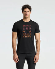 A man stands against a plain white background wearing the MENS CORTES GRAPHIC TEE - B6U328E200 by Psycho Bunny, which features a black T-shirt with an orange graphic of a skull and bunny ears.