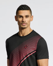 A person wearing a black Psycho Bunny MENS MACK SPORT TEE (B6U335E200) with a red geometric chest pattern stands against a plain background. The Moisture Wicking fabric complements their short, dark hair and neutral expression, highlighting both comfort and style.
