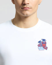 Wearing a Psycho Bunny Men's Puerto Rico Tee (B6U382F200) in white featuring palm trees, a long-eared creature, and "Isla del Encanto" in red and blue, paired with a thin silver necklace, exudes comfort and style—a subtle nod to Puerto Rican pride.