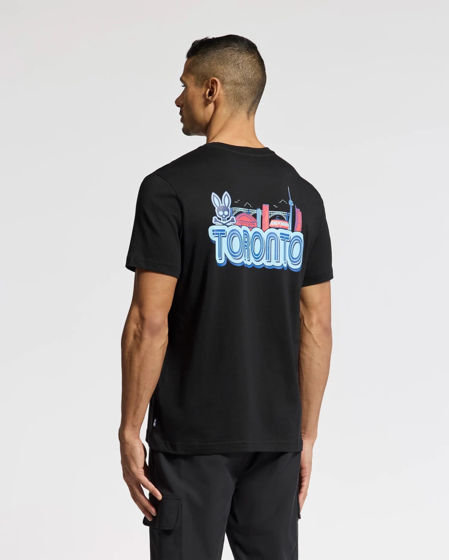 A person wears the Psycho Bunny MENS TORONTO TEE - B6U383F200, made of soft Pima cotton. It has a vibrant hometown hero graphic with "Toronto," a rabbit, and city landmarks on the back, perfectly showcased as they face away.