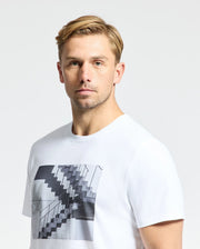 A man with short blond hair wears Psycho Bunny's MENS DEAN PHOTO REAL TEE - B6U390E200, made of soft Pima cotton and displaying an urban geometric monochrome graphic. He stands against a plain white background, looking directly at the camera.