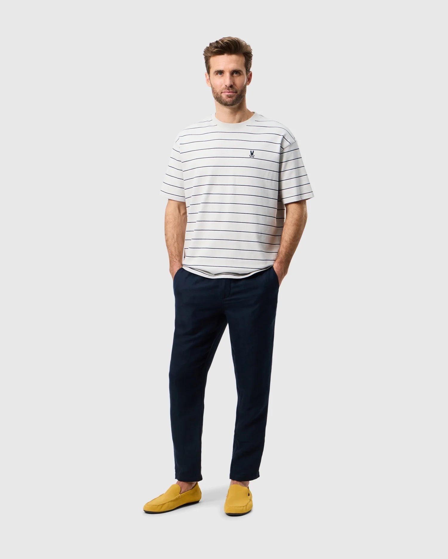 Head to toe view of a male model wearing the mens alton stripe heavy weight tee in pearl with both hands in his pockets