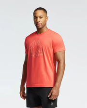 A man confidently stands in a coral Psycho Bunny MENS MELBOURNE GRAPHIC TEE B6U410F200, made from eco-friendly Peruvian Pima Cotton, with a bunny graphic. He pairs it with black shorts against a plain white background.