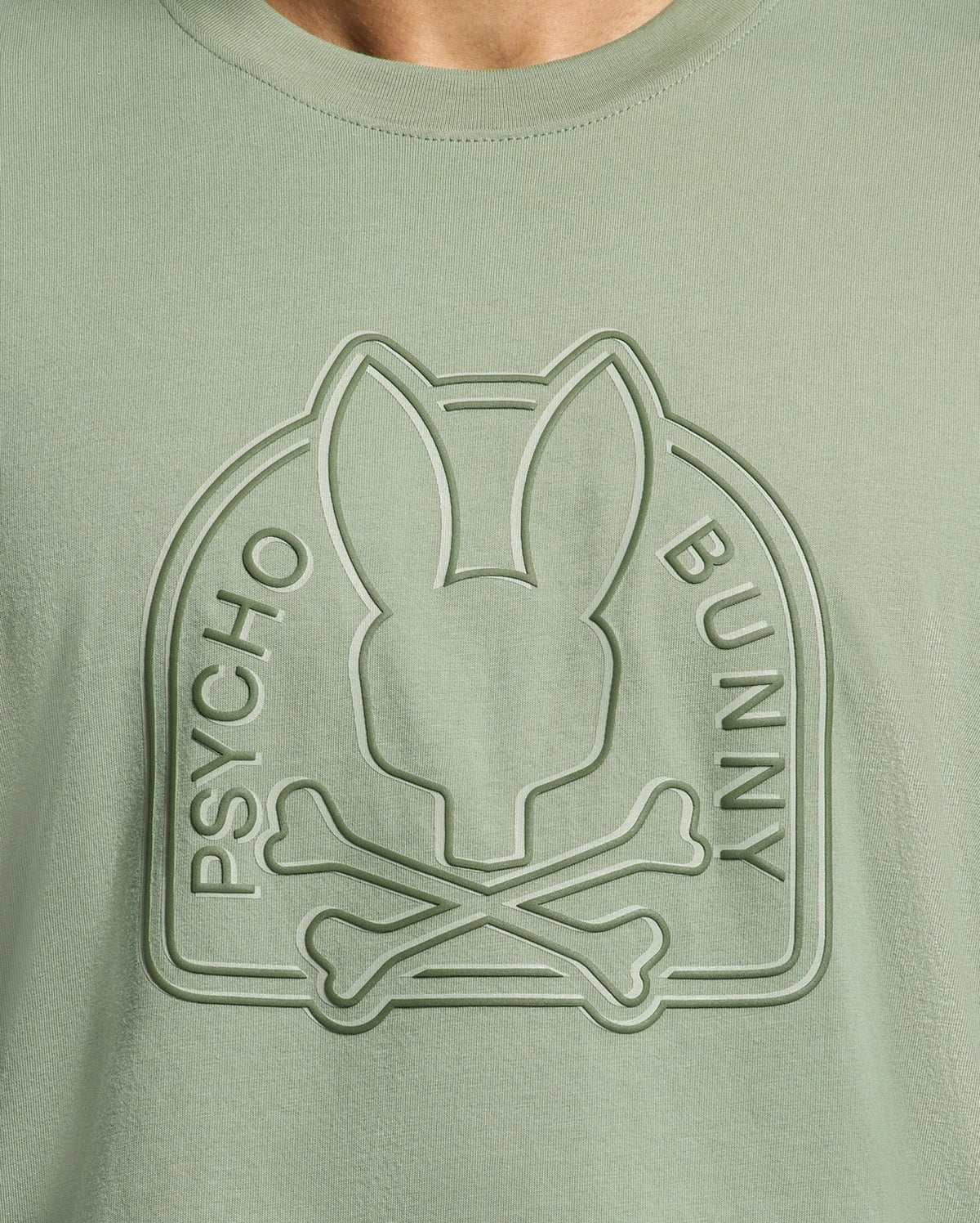 The MENS MELBOURNE GRAPHIC TEE - B6U410F200 by Psycho Bunny is a sage green shirt made from eco-friendly Peruvian Pima cotton, showcasing an embossed bunny head and crossed bones design encircled by "Psycho Bunny.