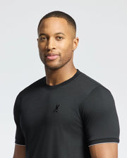 A man wearing the Psycho Bunny MENS BRYCE PERFORMANCE TEE - B6U490F200, made of Modal-Pima Cotton with a small logo, stands against a light gray background, looking at the camera with a neutral expression.