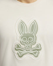 The Psycho Bunny MENS SYDNEY GRAPHIC TEE (B6U508F200) features a bold white bunny graphic with long ears blending into a skull over crossbones on a muted green background. Made from soft Pima cotton, it exemplifies unique and striking designs.