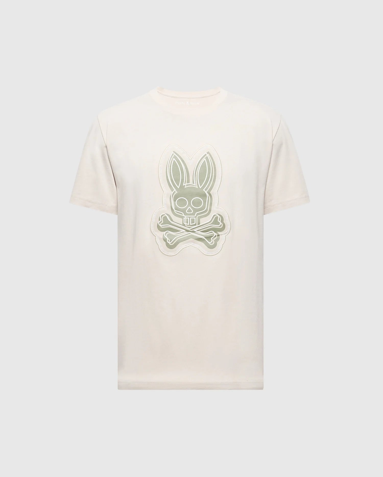 The MENS SYDNEY GRAPHIC TEE by Psycho Bunny features a cream-colored Pima cotton design with a stylized gray bunny and crossed bones logo on the front, set against a light gray background.