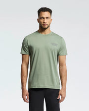 A man in a light green Psycho Bunny MENS SYDNEY BACK GRAPHIC TEE - B6U509F200 and black pants stands against a plain white background. The tee features a small logo on the left chest.